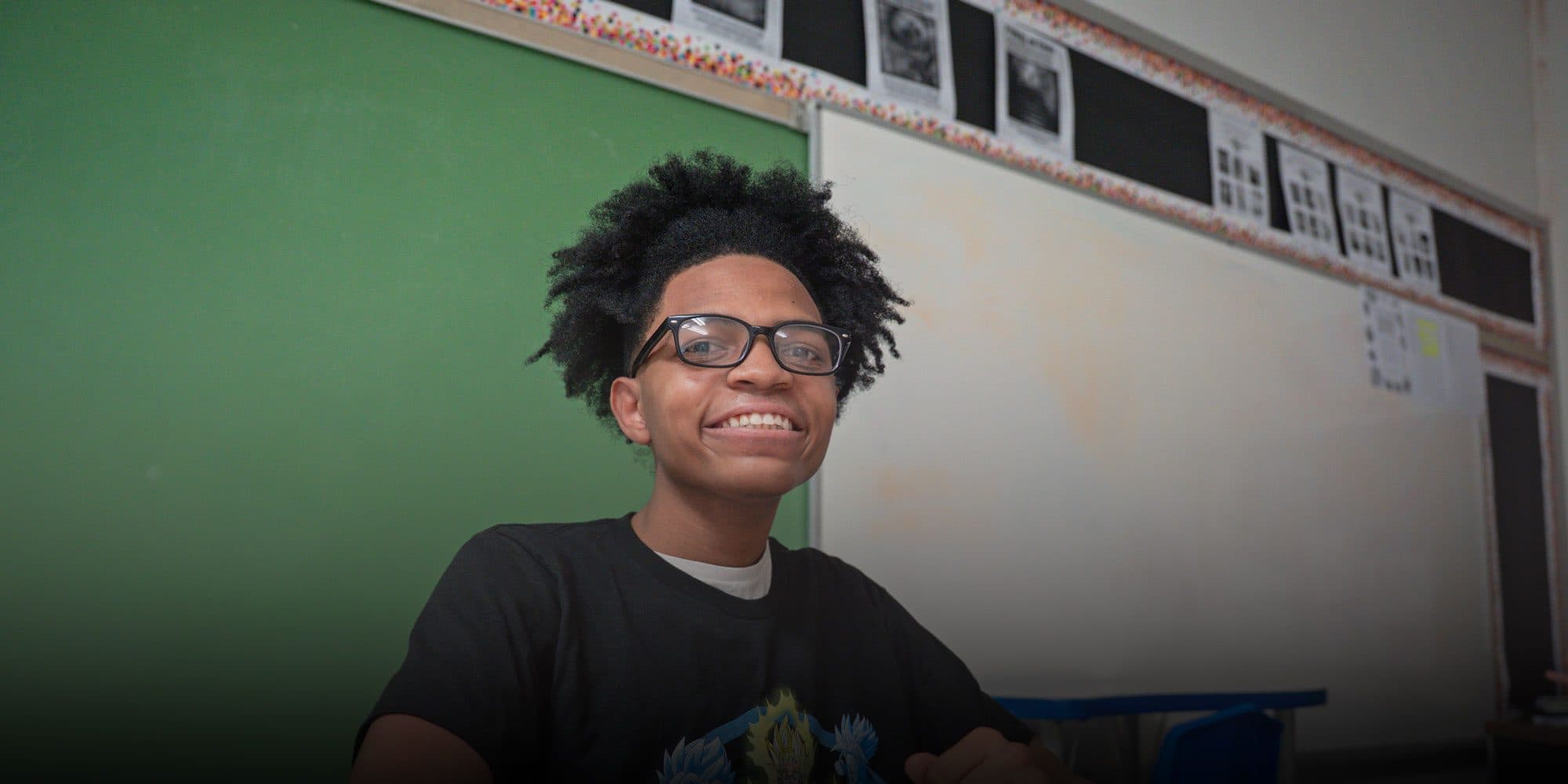 Smiling student wearing glasses in a classroom.