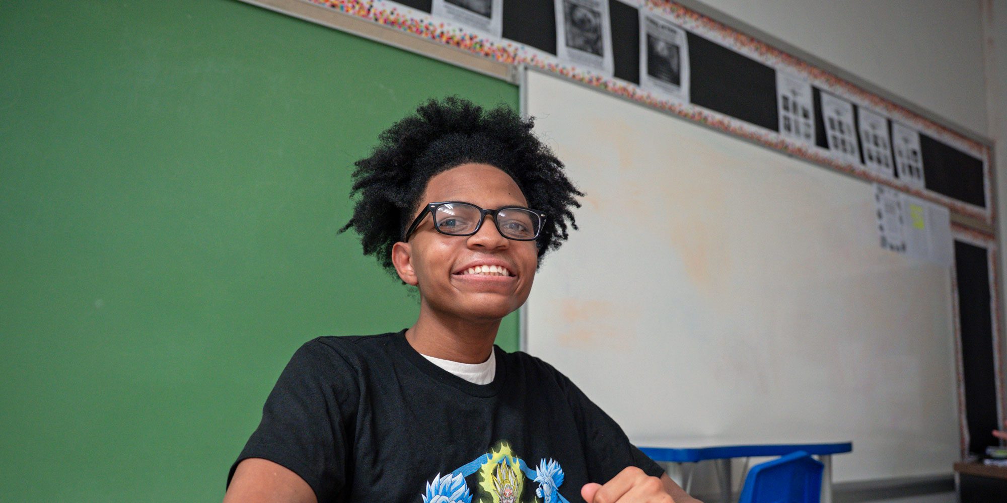 Smiling student wearing glasses in a classroom.