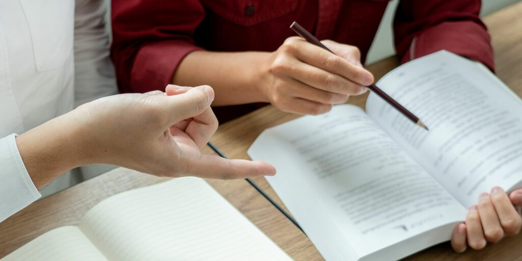 Close up image of an open book and teacher pointing out something to a student.