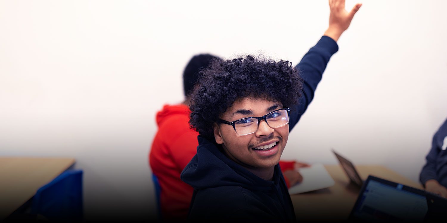 A high student sitting at desk with raised hand.